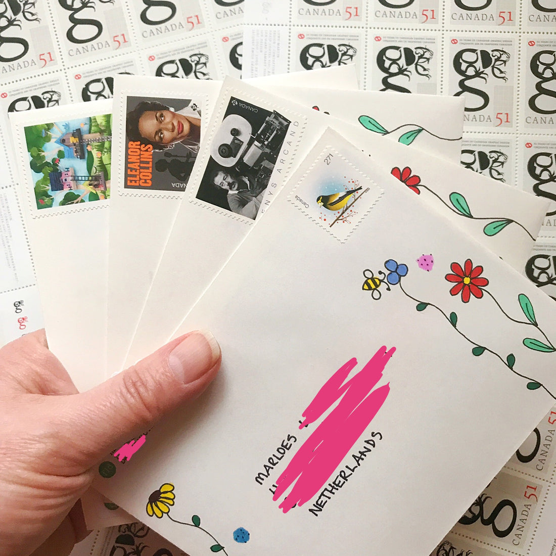 envelopes with Canadian stamps and floral doodles being help up against a background of sheets of Canadian stamps