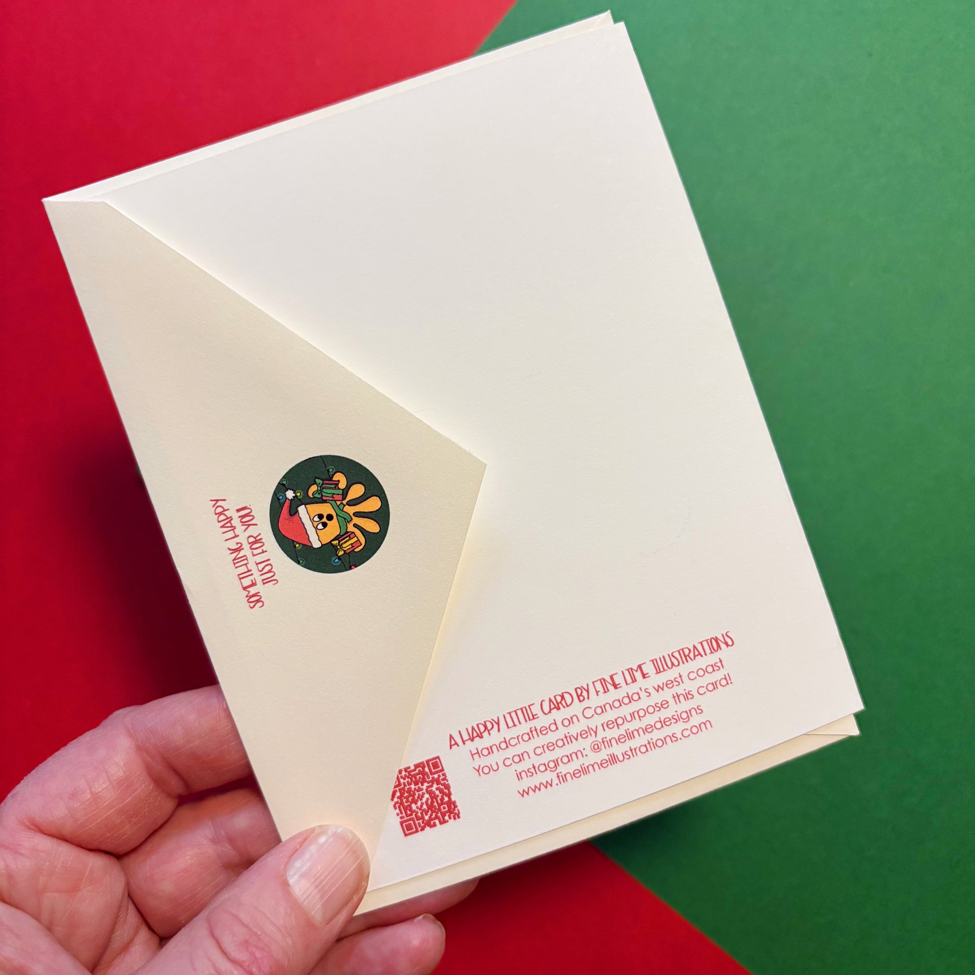 Hand holding a card and envelope to show the Christmas octopus illustration on the envelope flap and the text on the back of the card